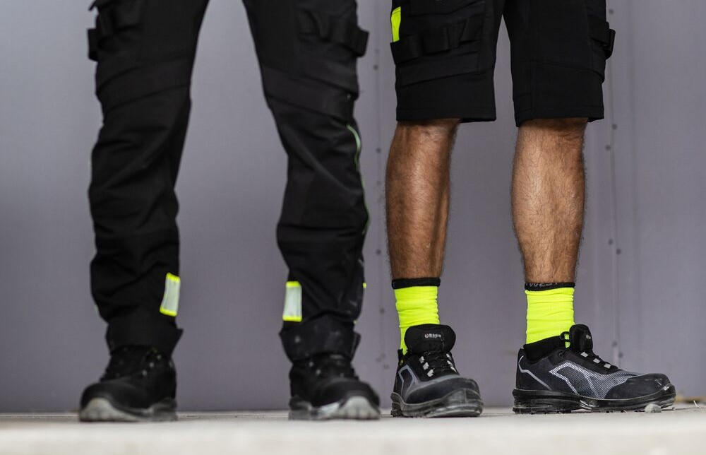 V&ecirc;em-se dois pares de pernas masculinas: um homem usa cal&ccedil;as de trabalho compridas pretas, o outro usa cal&ccedil;&otilde;es de trabalho curtos amarelos de alta visibilidade. Est&aacute; inclu&iacute;do um link para a nossa categoria de cal&ccedil;as de trabalho.