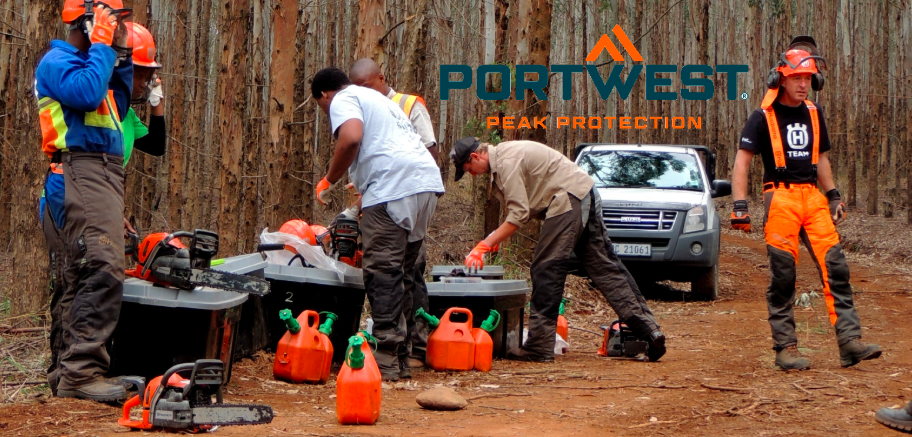 Trabalhadores florestais numa clareira a preparar-se para o trabalho com motosserra. O logótipo do fabricante, Portwest, em azul e laranja, está centrado acima da cena.