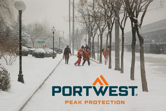 Calçada coberta de neve com pedestres amontoados, árvores e pessoas com roupas de alta visibilidade removendo a neve. Link para nossa coleção de inverno.