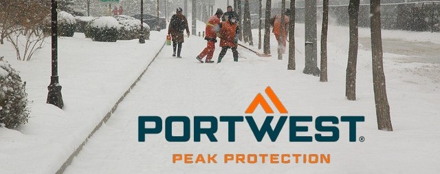 Calçada coberta de neve com pedestres amontoados, árvores e pessoas com roupas de alta visibilidade removendo a neve.