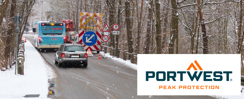 Cena de canteiro de obras com ônibus e carro em uma estrada nevada cercada por árvores. No canto direito encontra-se o logótipo da marca Portwest.