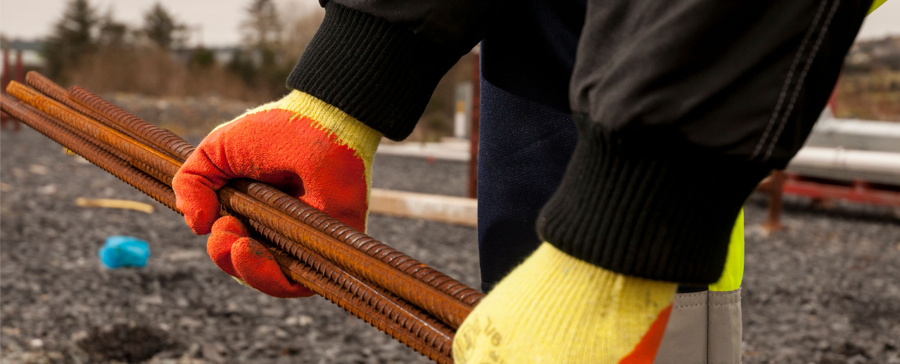 Imagem do modelo da luva Fortis Grip A150 em amarelo/laranja trabalhando com vergalhão.