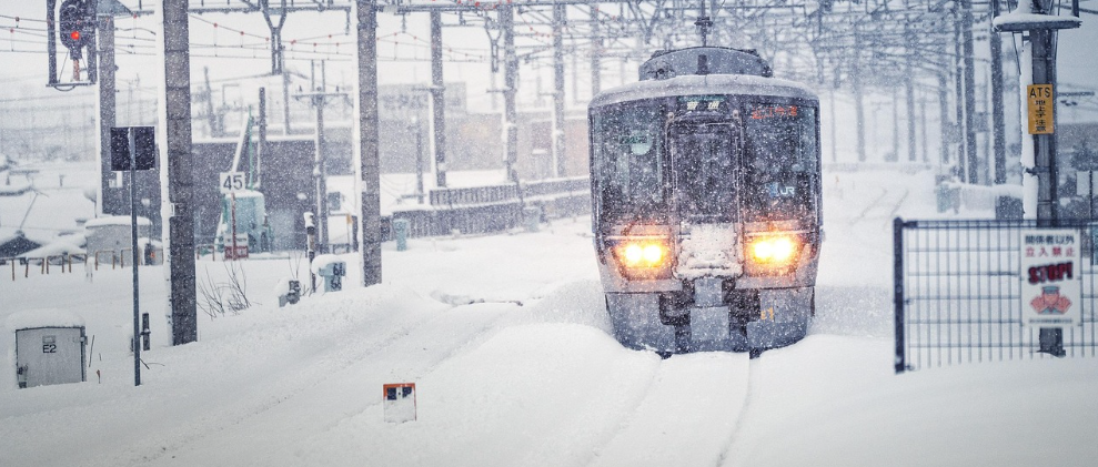 Vista frontal de um comboio. Os carris est&atilde;o cobertos de neve e a visibilidade &eacute; fraca devido &agrave; queda de neve.