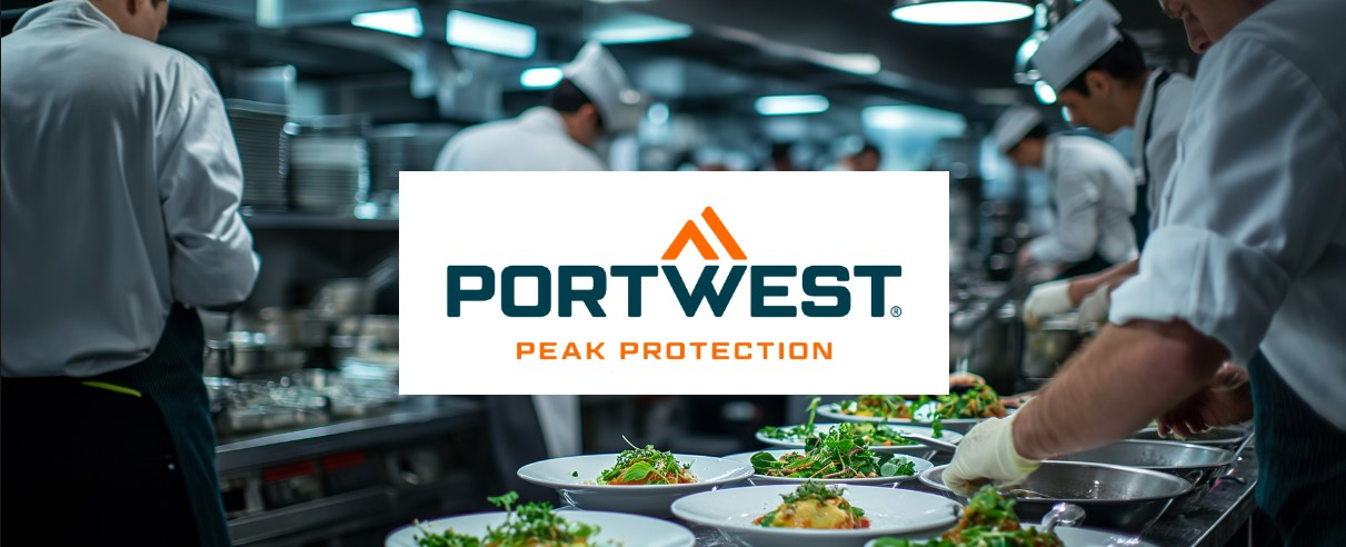 Uma cozinha comercial com vários chefs com uniformes brancos a trabalhar em diferentes estações e a organizar a comida em pratos. O foco está nos pratos preparados na hora. O logótipo "Peak Protection" da Portwest está colocado centralmente acima da imagem.