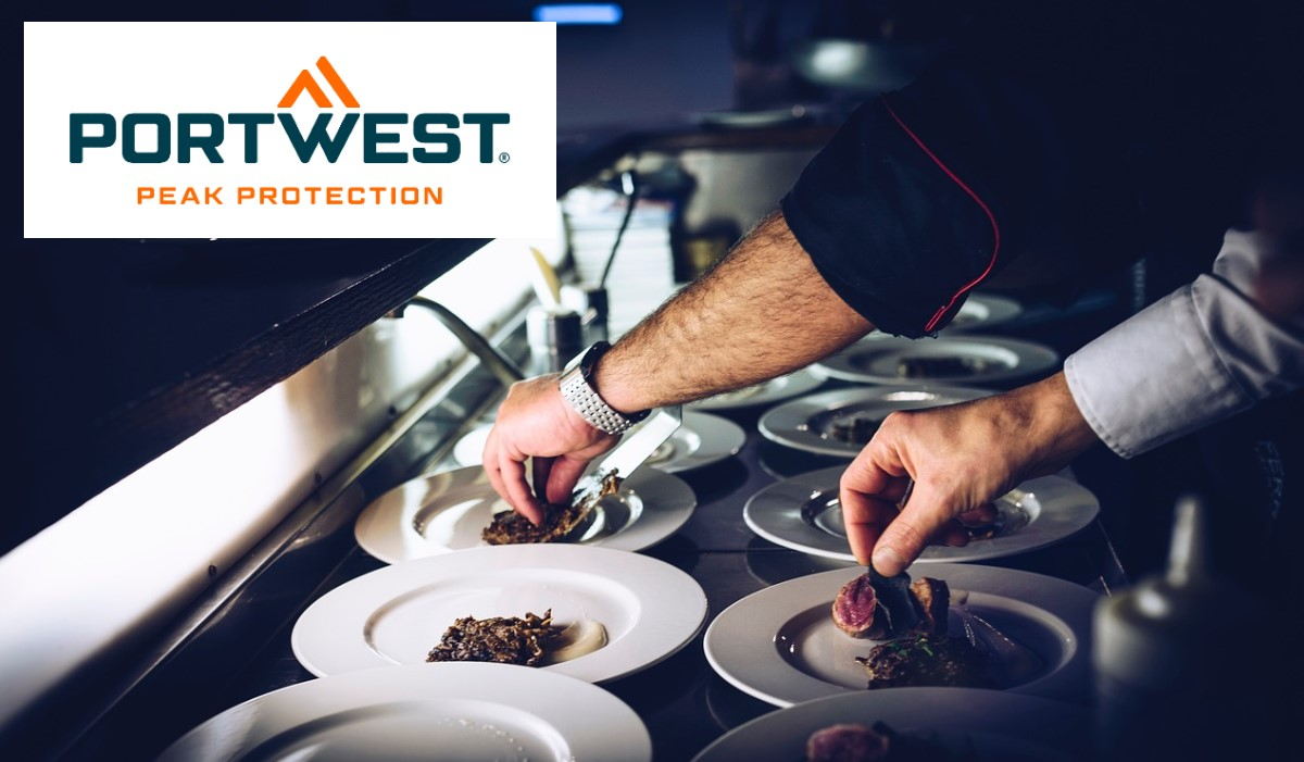 Dois chefs, cada um com um braço a usar um casaco preto de chef e o outro com um branco, arrumam cuidadosamente a comida em pratos brancos numa cozinha profissional. O logótipo "Peak Protection" da Portwest é apresentado no canto superior esquerdo. Há um link que leva às roupas do nosso chef.