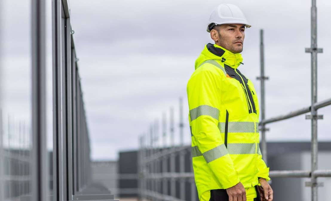 Trabalhadores com roupa de trabalho amarela de alta visibilidade com capacete branco em frente a uma janela e na parte superior de um andaime com ligação à coleção DX4.