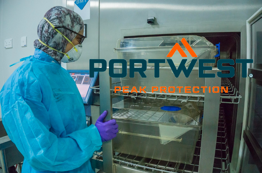 Pessoa com roupa descartável azul de laboratório em frente a um armário de aço inoxidável. O logotipo do fabricante Portwest em laranja e azul está no lado direito da imagem. Um link para nossas roupas de laboratório está incluído.