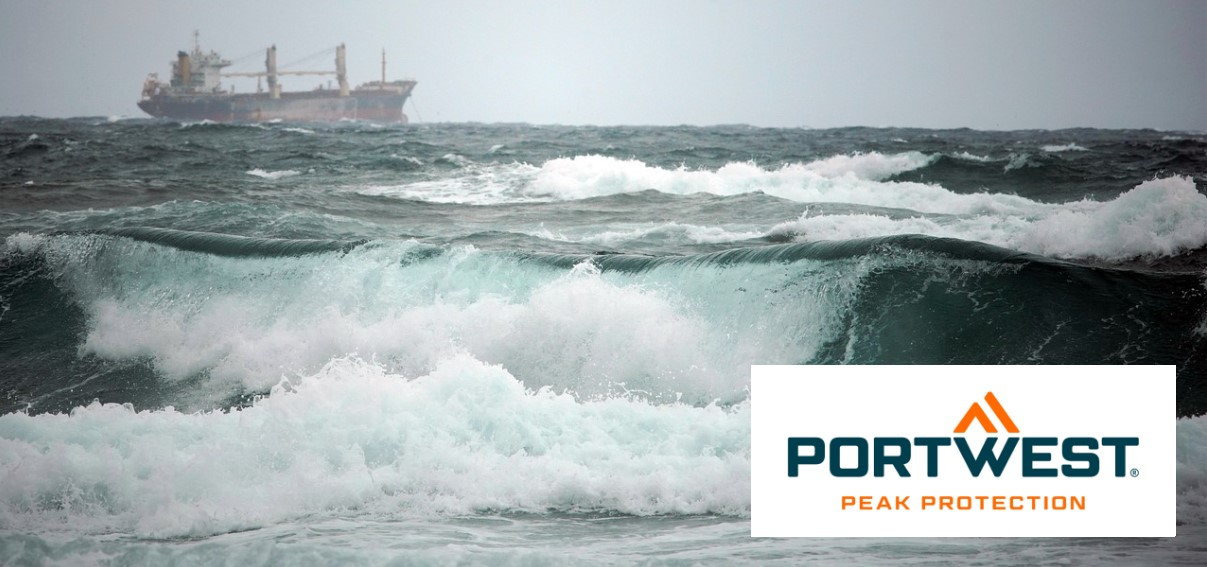 Um navio de carga à distância navega num mar tempestuoso com ondas altas e cobertas de espuma. Ondas fortes e turbulentas podem ser vistas em primeiro plano. O logótipo da Portwest está no canto inferior direito da imagem.
