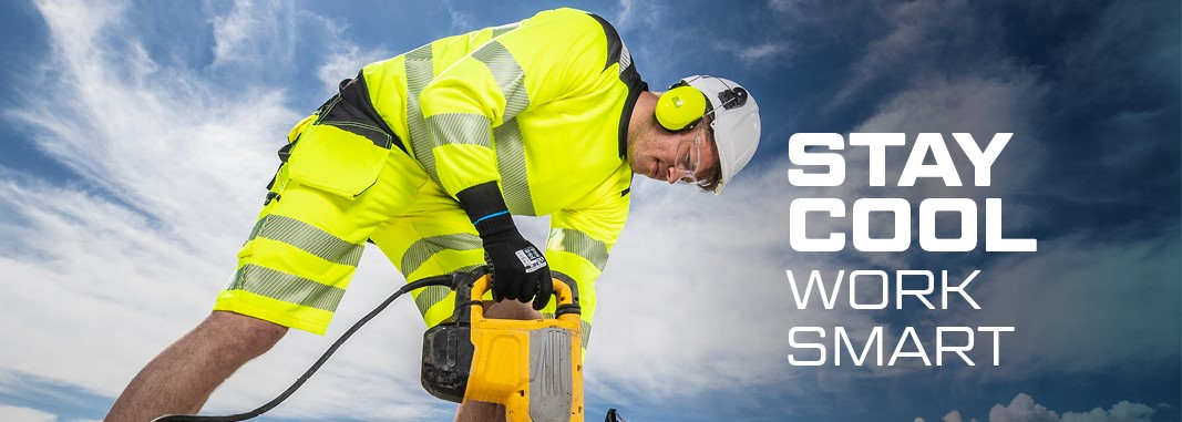 Trabalhador com capacete e proteção auditiva em roupas de trabalho de verão amarelo de alta visibilidade trabalhando com uma britadeira, ao fundo azul, céu ligeiramente nublado, escavadeira e pilha de pranchas de madeira.