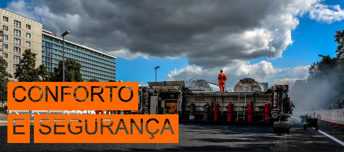 Cena de um estaleiro de obras de uma estrada. À esquerda da foto podem ver-se edifícios altos e algumas árvores, a parte direita da foto está coberta por uma fonte de água. No canto inferior esquerdo da imagem estão as palavras “Conforto e Segurança” em letras recortadas com fundo laranja.