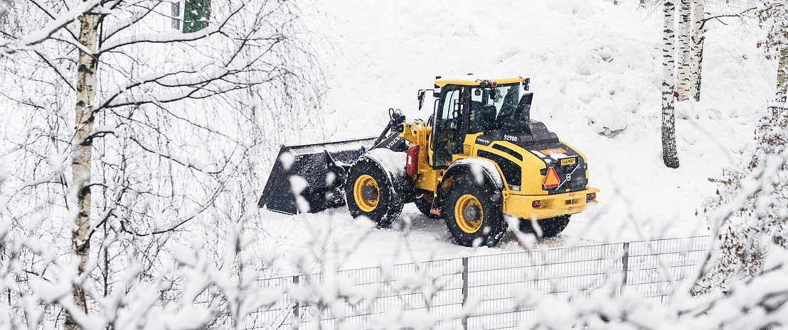 Trator amarelo com pá na paisagem nevada com cercas e bétulas.