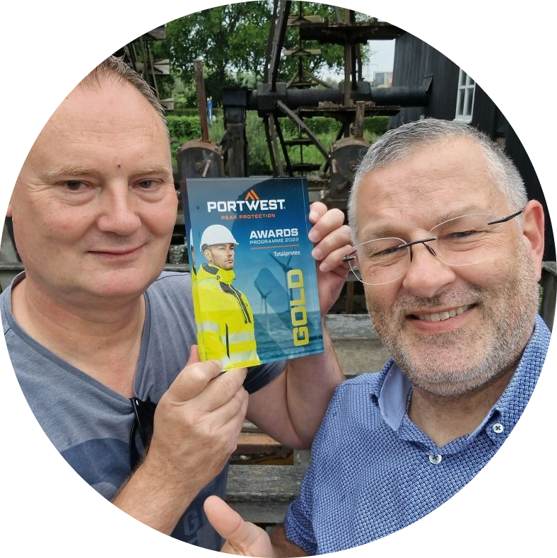 Sjoerd Kusters e Patrick Kits num cenário rural. Os homens sorriem para a câmera, Sjoerd segura a placa dourada nas mãos, Patrick levanta o polegar direito.